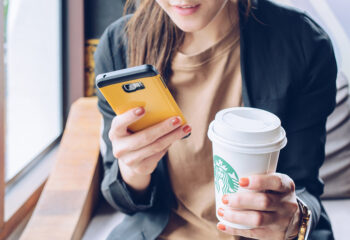 Image shows woman holding mobile phone and cuts of coffee from Starbucks.