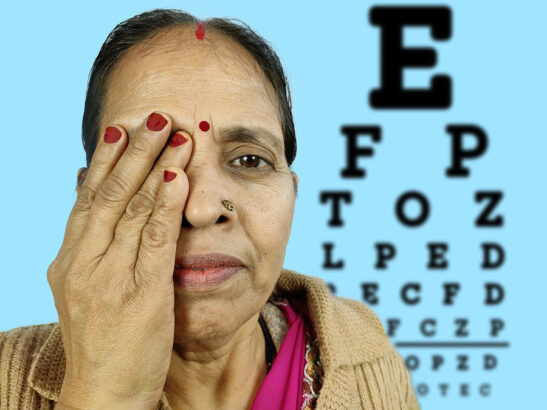Image shows woman looking at eye chart with one eye covered.