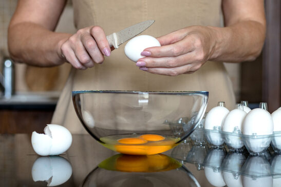Image shows Woman breaking eggs into bowl.