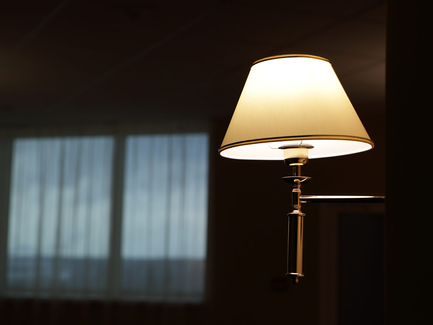 A stand lamp with the light on in a dark living room.