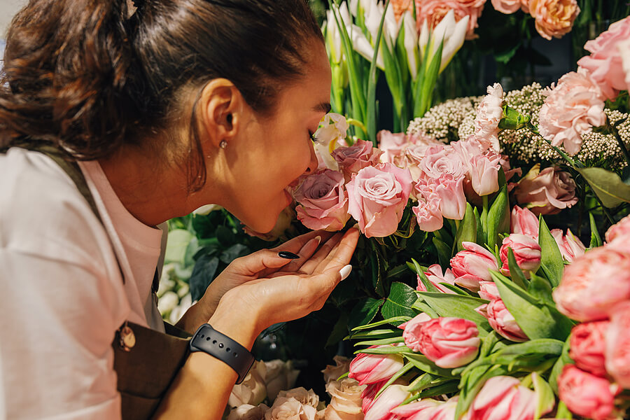 Image shows woman smelling flowers.