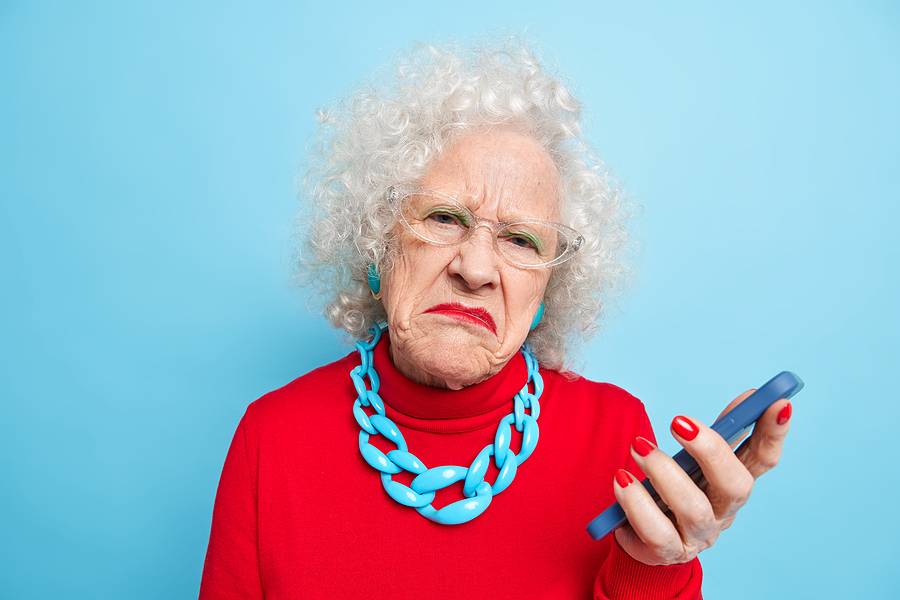 Older woman looks at mobile phone with dismayed expression.