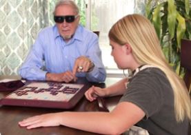 Man wearing Eyedaptic glasses playing scrabble with granddaughter