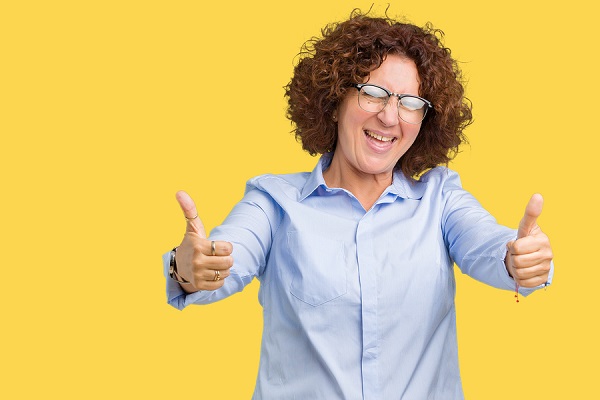 Happy woman wearing glasses giving thumbs up on a yellow background.