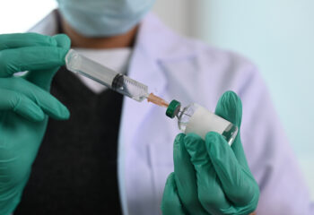 Closeup of doctor’s gloved hands holding needle syringe